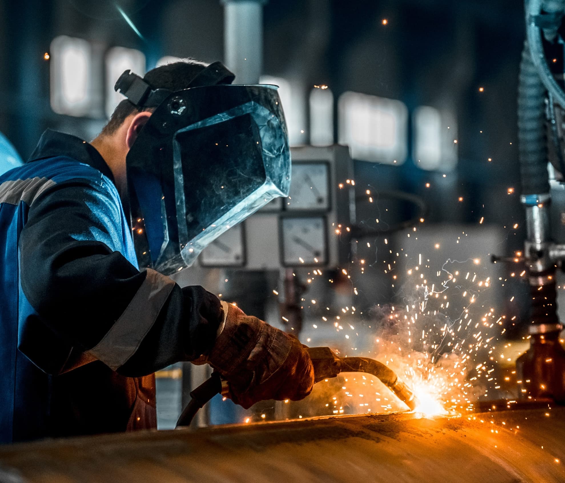 Welder at work in an industrial setting, sparks and light from welding